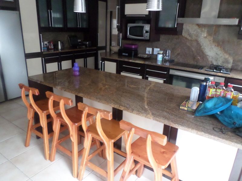 A functional kitchen featuring granite countertops, built-in cabinetry, a gas hob with extractor fan, and a built-in microwave, complemented by tiled flooring.