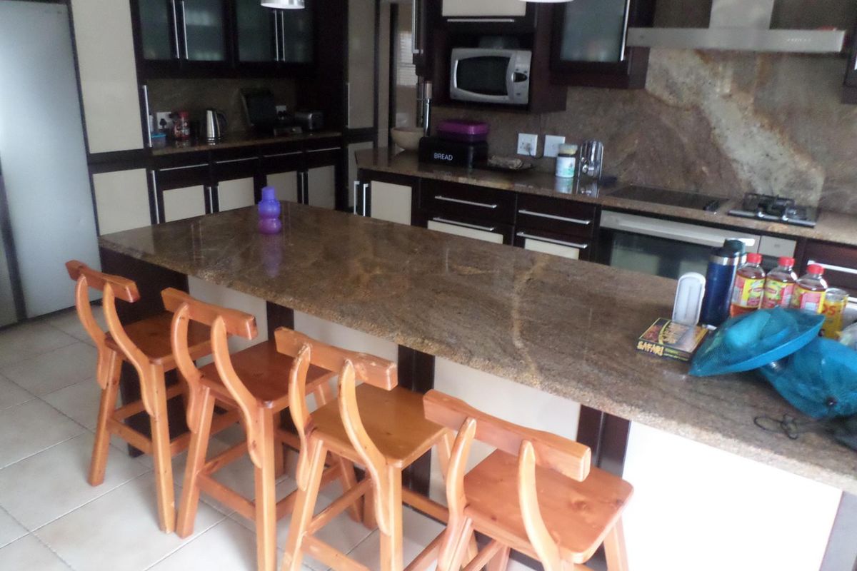 A functional kitchen featuring granite countertops, built-in cabinetry, a gas hob with extractor fan, and a built-in microwave, complemented by tiled flooring.