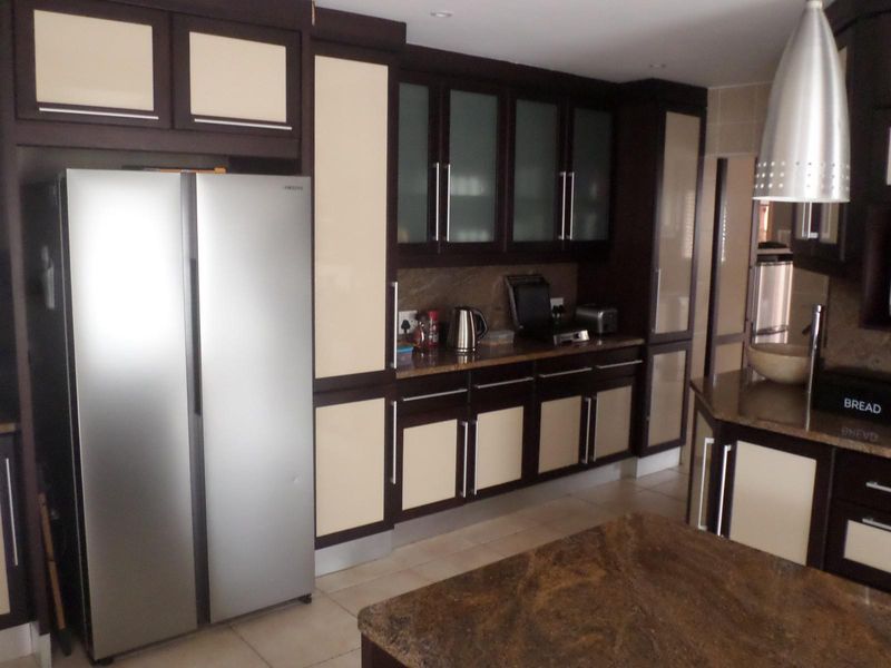 A well-appointed kitchen featuring dark wood cabinetry with cream panels, granite countertops, tiled flooring, and modern pendant lighting.