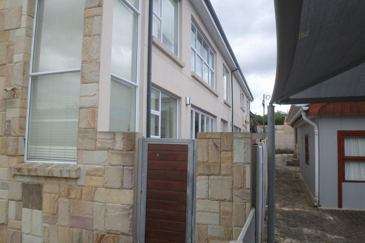 A side view of the property featuring stone cladding, modern aluminium windows, and a paved pathway with a shade sail structure.