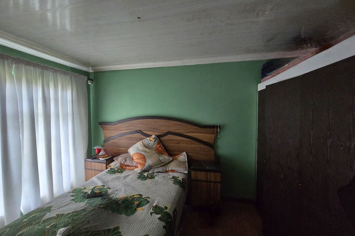 A bedroom featuring wooden flooring, a built-in wardrobe, and visible ceiling water damage requiring repair.