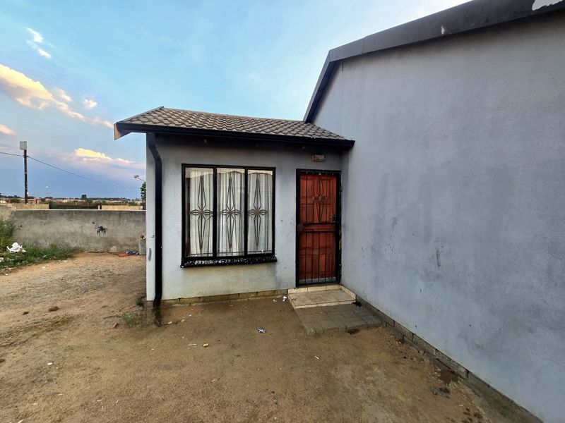 Rear exterior view of the house featuring a security gate, window security bars, and a tiled roof, set against a concrete perimeter wall.