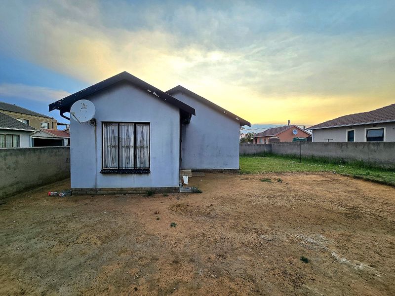 Rear view of the property featuring a simple facade, perimeter wall, and an expansive, unlandscaped yard area at sunset.
