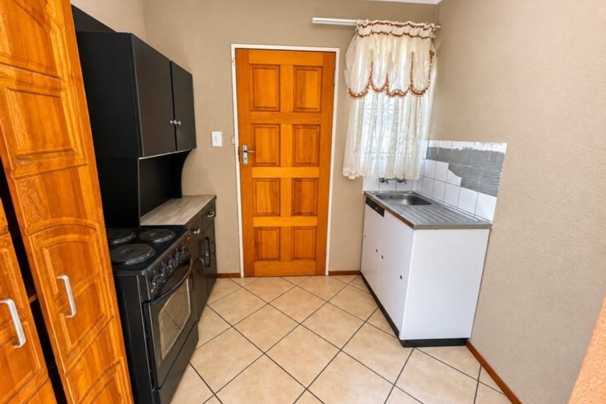 Compact kitchen featuring built-in oven, electric hob, stainless steel sink, and tiled flooring, requiring minor cosmetic updates to complete the wall tiling and finishes.