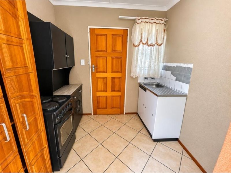Compact kitchen featuring built-in oven, electric hob, stainless steel sink, and tiled flooring, requiring minor cosmetic updates to complete the wall tiling and finishes.