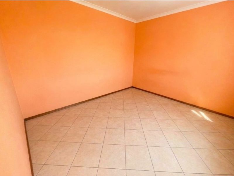 An empty bedroom featuring tiled flooring and bright orange walls, providing a blank canvas for personalization.
