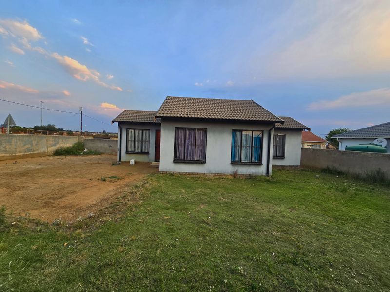 A detached single-story house featuring a tiled roof and security bars on windows, set on a spacious plot with a perimeter wall.