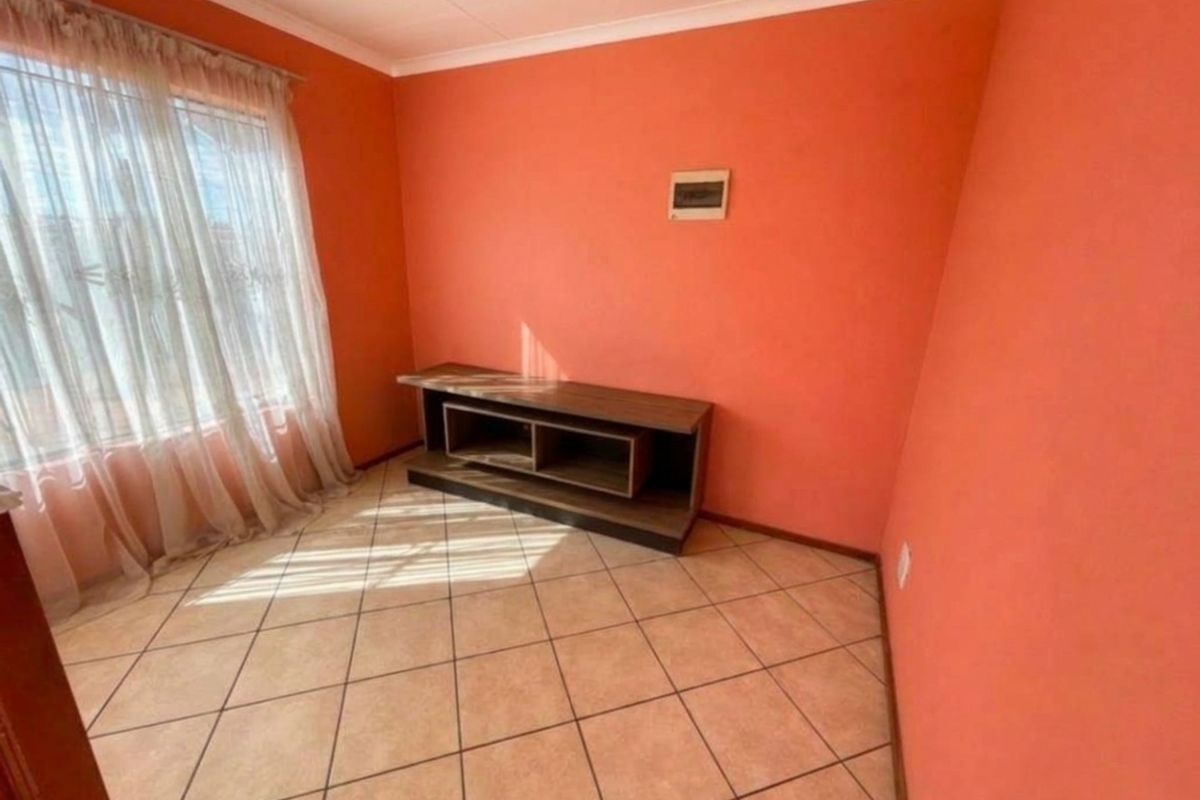 A living room featuring ceramic floor tiles, coved ceilings, and a large window with sheer curtains, providing a neutral base for interior design updates.