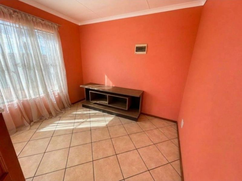 A living room featuring ceramic floor tiles, coved ceilings, and a large window with sheer curtains, providing a neutral base for interior design updates.