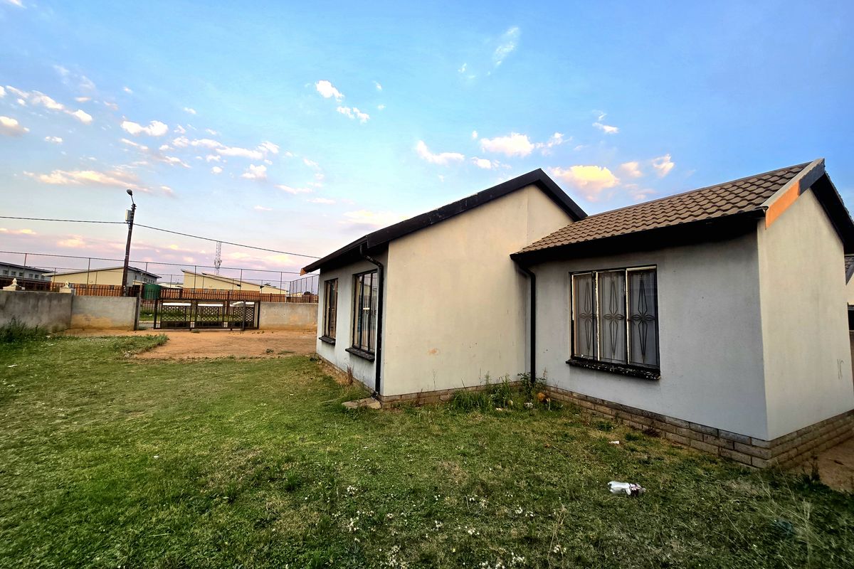 Rear view of a single-story house featuring a tiled roof, security-barred windows, and a surrounding perimeter wall with a metal gate.