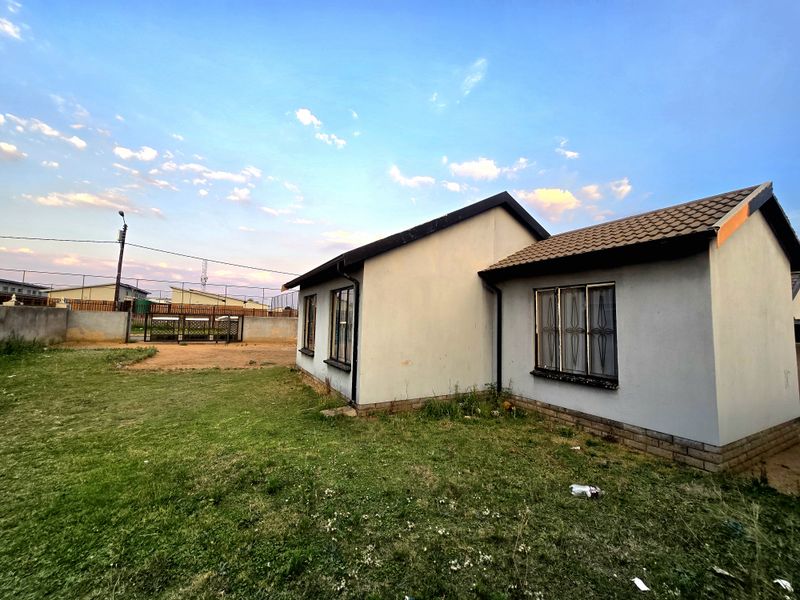 Rear view of a single-story house featuring a tiled roof, security-barred windows, and a surrounding perimeter wall with a metal gate.
