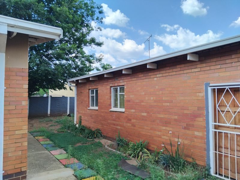 Rear exterior view of a brick house featuring a concrete pathway, security gate, and established garden area.
