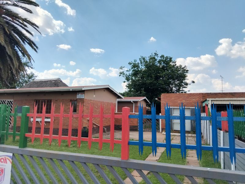 Front view of a face brick house featuring a thatch roof, a paved driveway, and a multi-colored metal security fence.