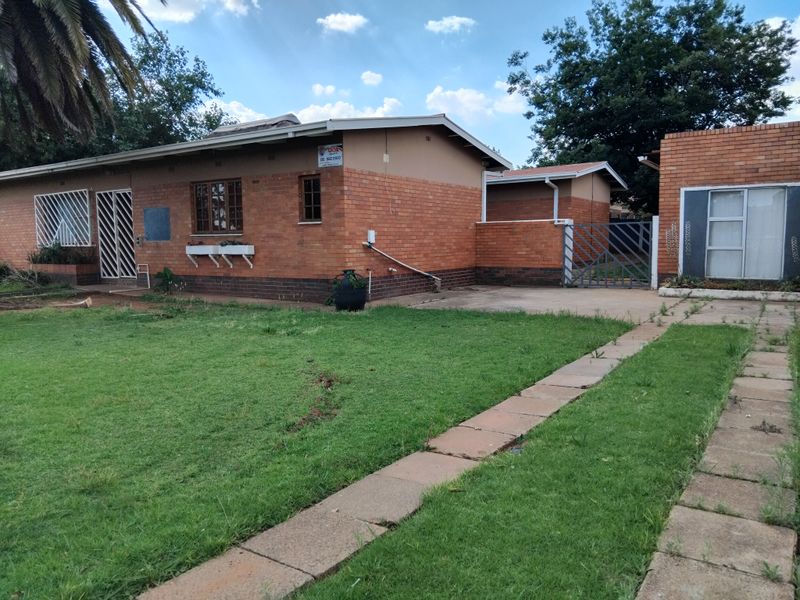 Front view of a single-story face-brick house featuring a paved driveway, security gates, and a spacious front lawn.
