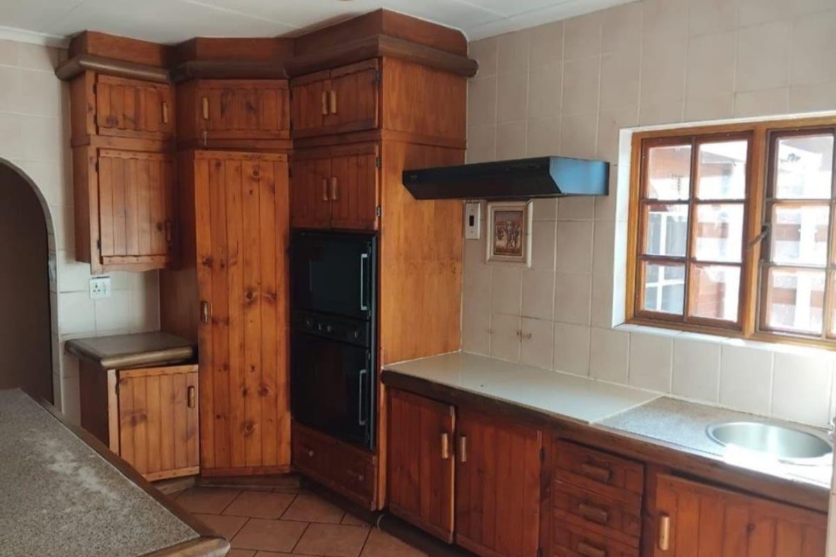 A traditional kitchen featuring extensive built-in wooden cabinetry, a built-in oven, extractor fan, and tiled splashbacks with a functional sink area.