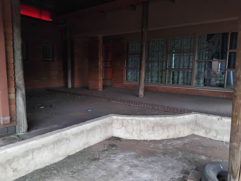 A covered outdoor patio area featuring brick and timber structural elements, requiring maintenance and cleaning to restore its functional appeal.