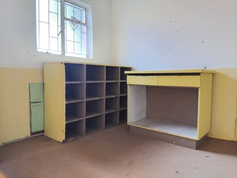 A utility or storage room featuring built-in shelving and counter space, requiring cosmetic updates and wall repairs.