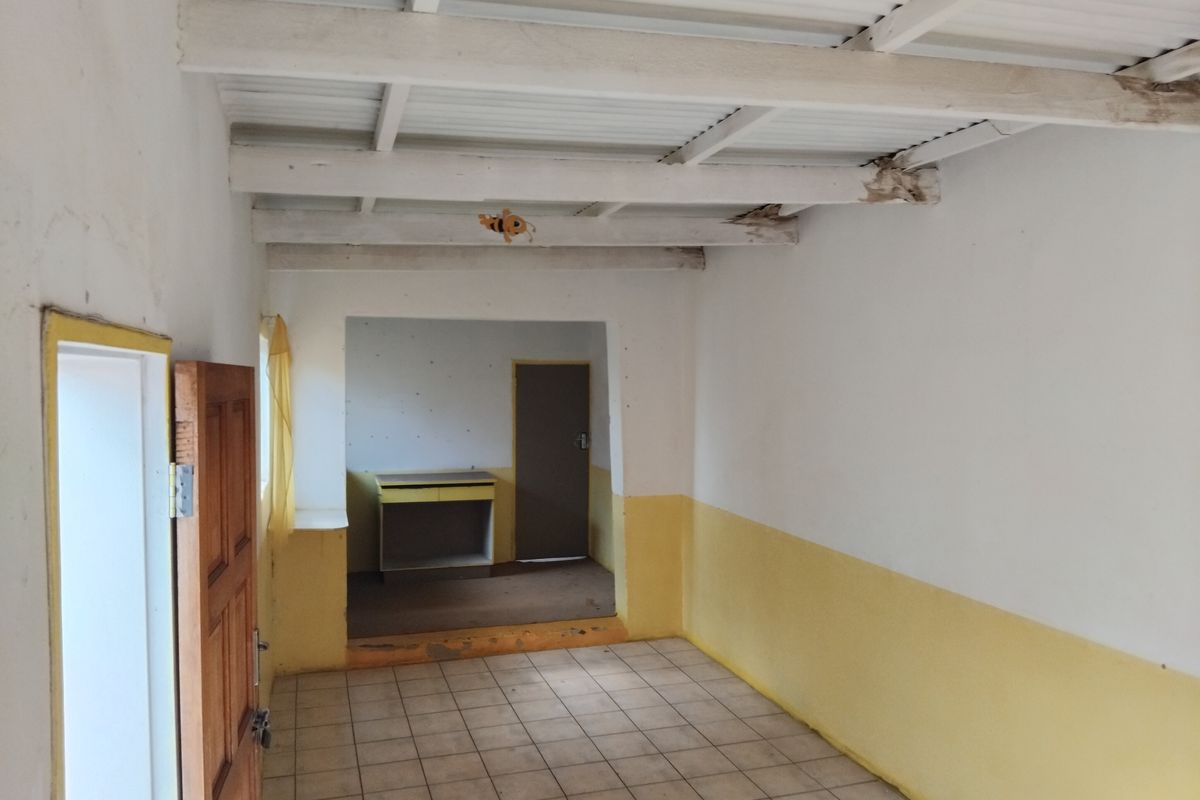 An empty living area featuring exposed timber ceiling beams, ceramic floor tiles, and a secondary room access with built-in cabinetry.