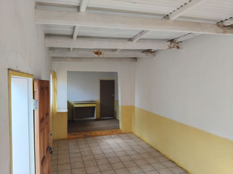 An empty living area featuring exposed timber ceiling beams, ceramic floor tiles, and a secondary room access with built-in cabinetry.