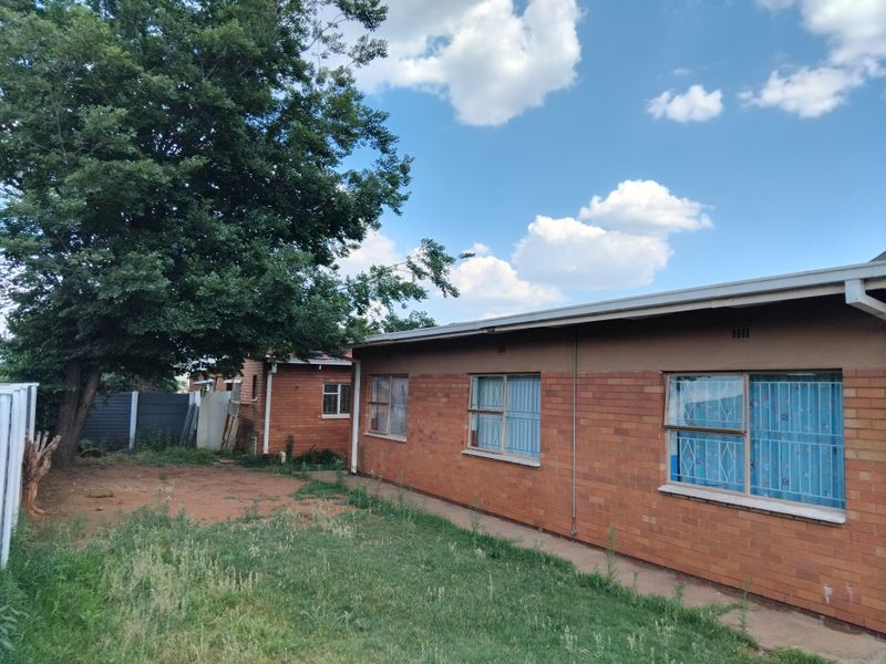 Rear view of a single-story brick house featuring security bars on windows and an expansive garden area.
