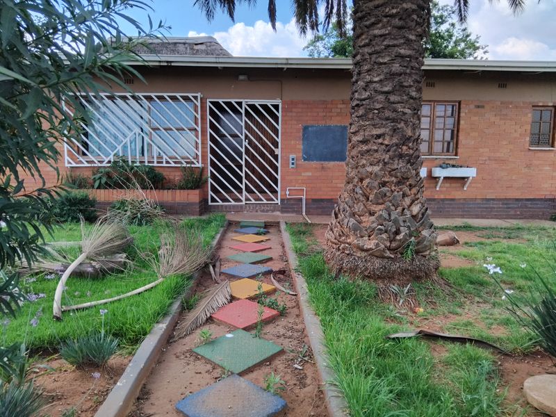 Front elevation of a face brick house featuring security gates, bars, and a thatched roof, set within a garden with a paved walkway.