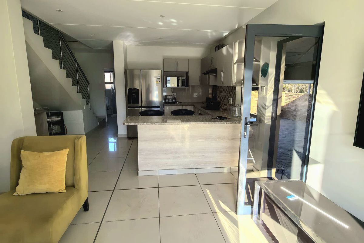 Open plan living area featuring a modern kitchen with granite countertops, tiled flooring, and direct access to an outdoor patio through a glass door.
