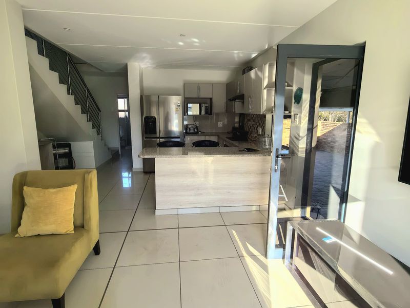 Open plan living area featuring a modern kitchen with granite countertops, tiled flooring, and direct access to an outdoor patio through a glass door.