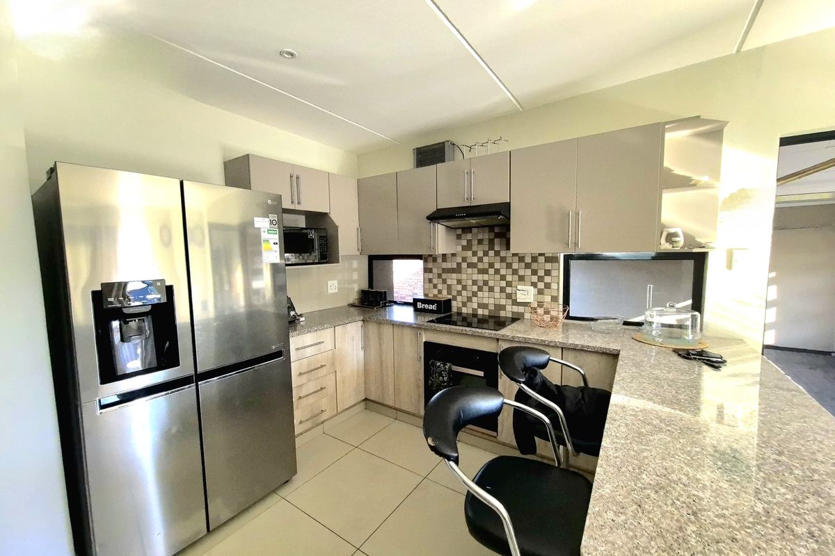 Modern kitchen featuring granite countertops, built-in oven, electric hob, extractor fan, and a functional breakfast bar with tiled flooring.