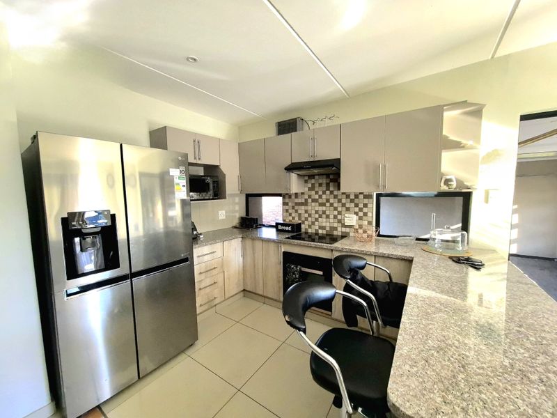 Modern kitchen featuring granite countertops, built-in oven, electric hob, extractor fan, and a functional breakfast bar with tiled flooring.