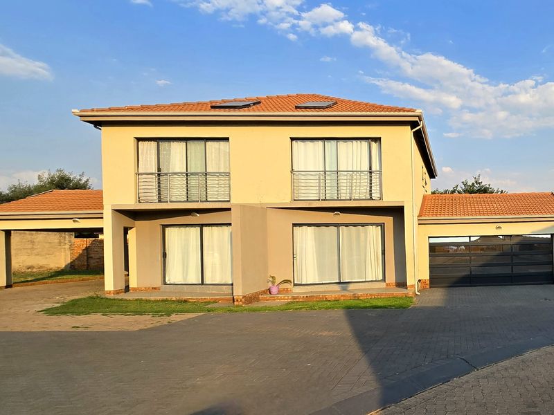 A modern two-story residential property featuring a terracotta tiled roof, solar panels, sliding glass doors with balconies, and an integrated garage.