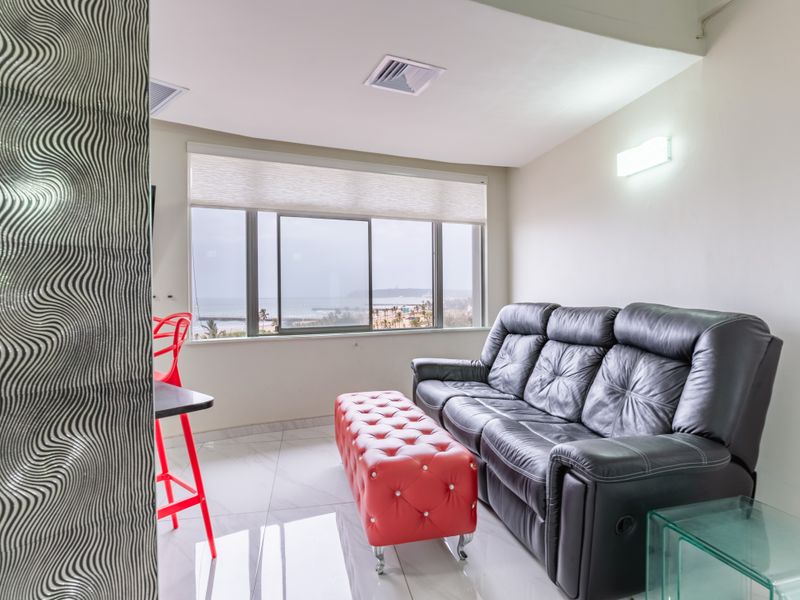 A bright living room featuring polished tiled flooring, a textured feature wall, and large sliding windows offering scenic coastal views.