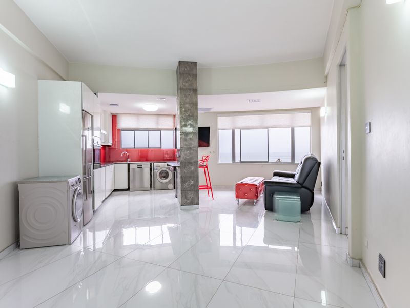 Modern open-plan living area featuring a sleek kitchen with glossy cabinetry, red glass splashback, and polished porcelain floor tiles throughout.