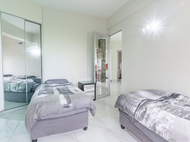 A bright bedroom featuring polished tiled flooring and a large mirrored sliding wardrobe, offering a clean and modern aesthetic.