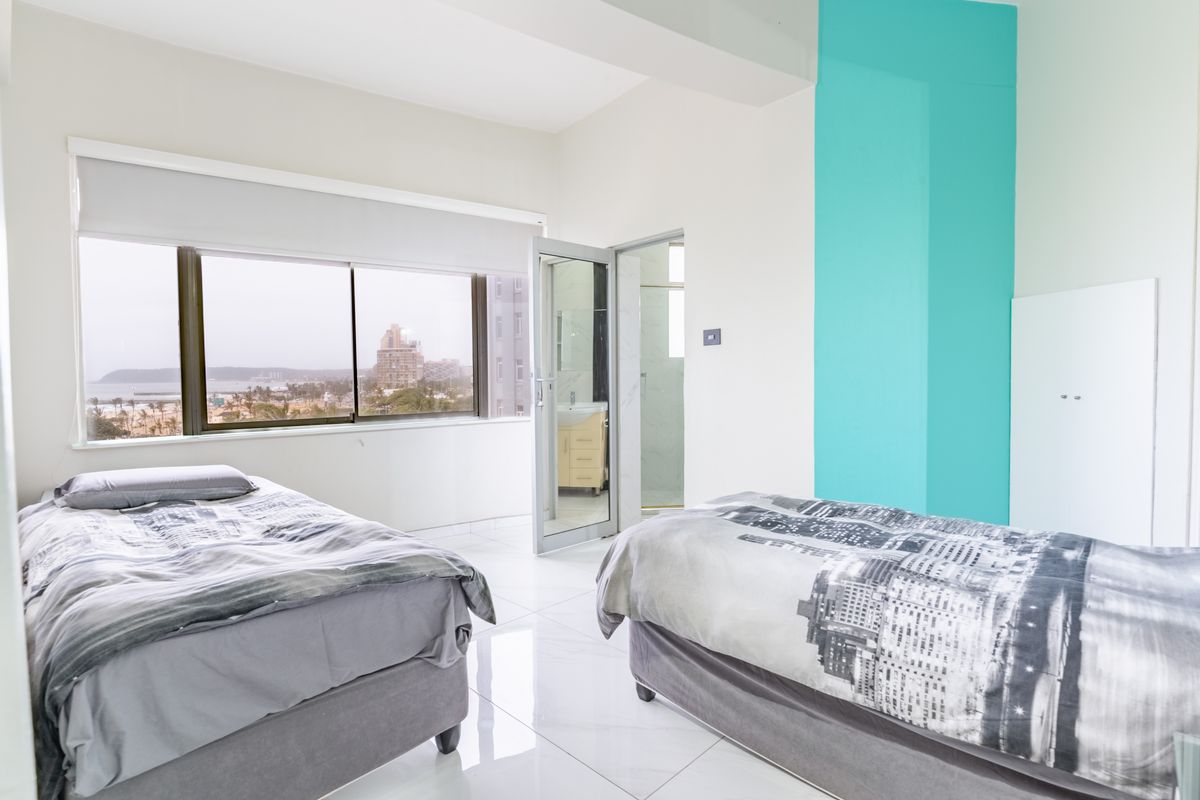 Spacious bedroom featuring large windows with coastal views, tiled flooring, and direct access to an en-suite bathroom.
