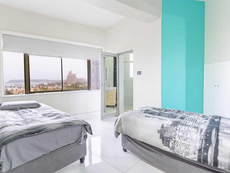 Spacious bedroom featuring large windows with coastal views, tiled flooring, and direct access to an en-suite bathroom.