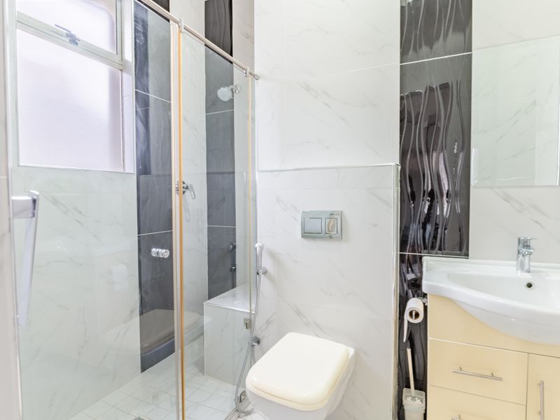 Modern bathroom featuring a glass-enclosed shower with a built-in bench, wall-mounted toilet, and a vanity cabinet with a ceramic basin.