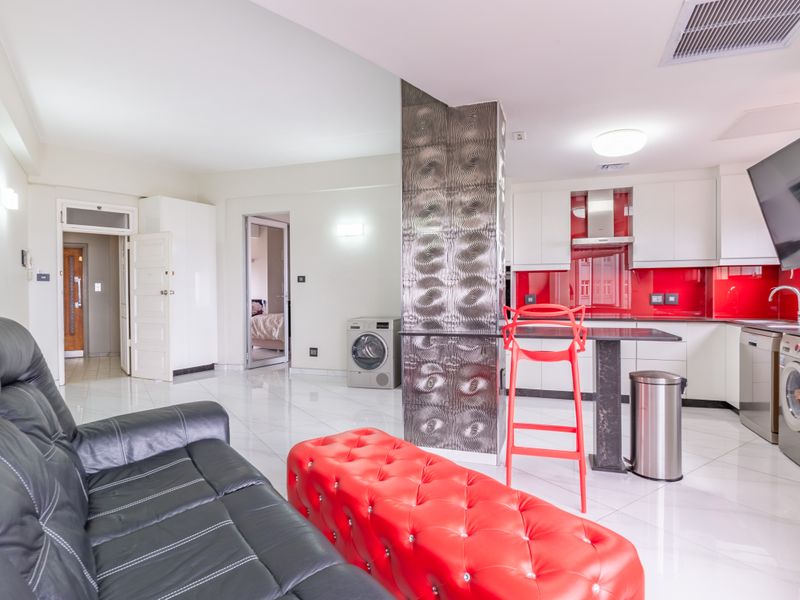 Modern open-plan living area featuring a sleek kitchen with red glass splashback, high-gloss cabinetry, and polished porcelain floor tiles throughout.