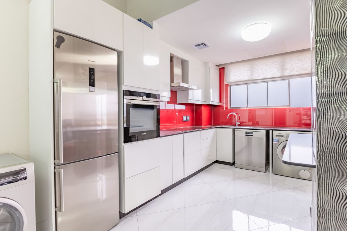 Modern kitchen featuring high-gloss white cabinetry, vibrant red glass splashback, integrated appliances, and polished marble-look floor tiles.