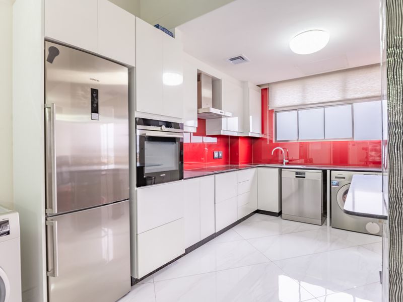 Modern kitchen featuring high-gloss white cabinetry, vibrant red glass splashback, integrated appliances, and polished marble-look floor tiles.