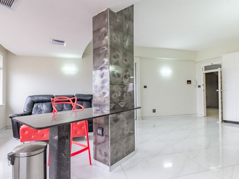 Modern open-plan living area featuring polished marble-look flooring, a central decorative tiled structural column, and a built-in breakfast bar.