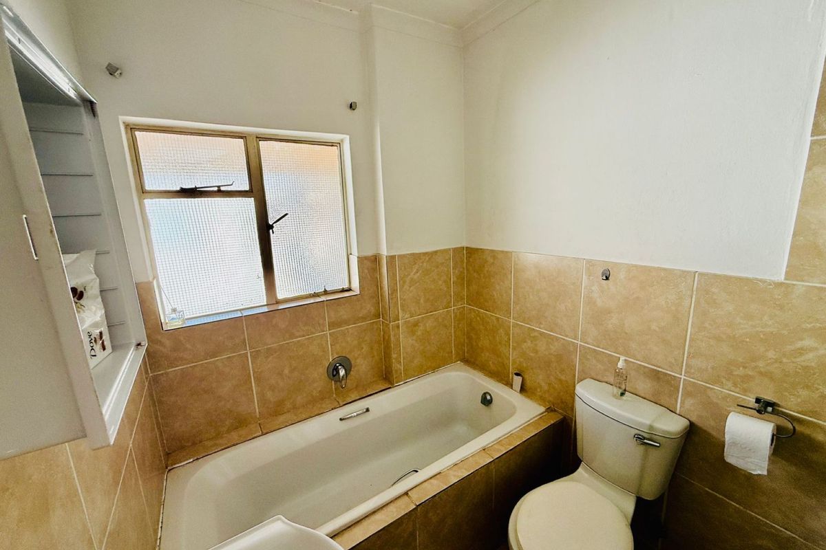 A functional bathroom featuring a built-in bathtub with tiled surround, a standard toilet, and a window providing natural light.