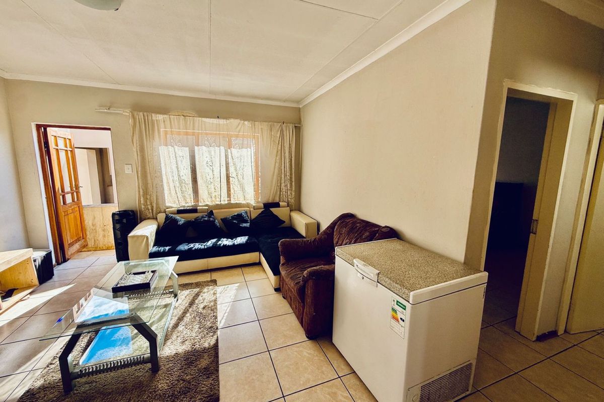 A living room featuring tiled flooring, natural light from a window, and access to adjacent rooms, providing a functional and open living space.