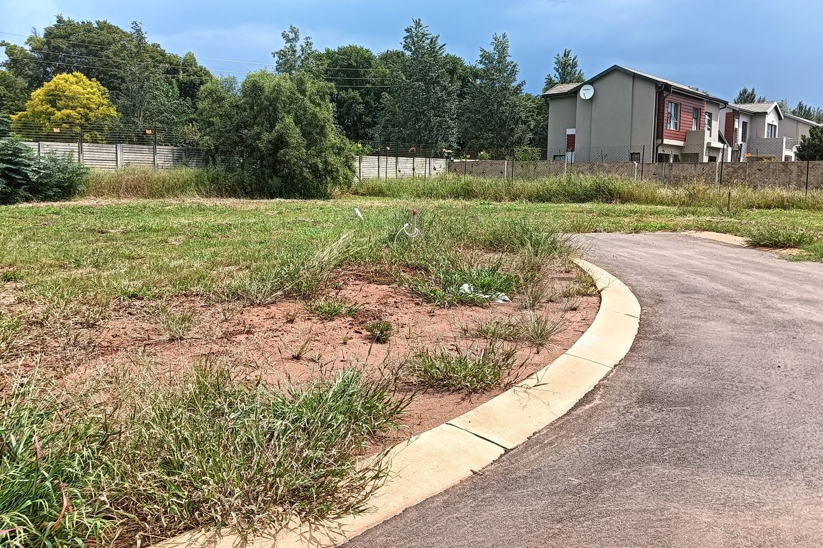 A vacant residential plot featuring a paved driveway, concrete curbing, and perimeter fencing, ready for development.