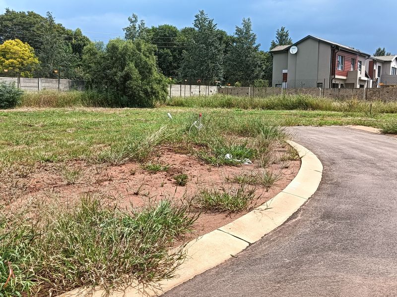 A vacant residential plot featuring a paved driveway, concrete curbing, and perimeter fencing, ready for development.
