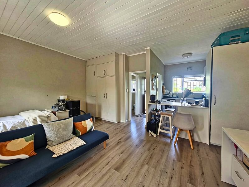 Open-plan living area featuring laminate flooring, a timber ceiling, built-in cupboards, and a functional breakfast bar connecting to the kitchen space.