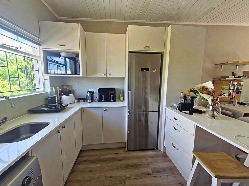 A compact, modern kitchen featuring white cabinetry, stainless steel appliances, laminate flooring, and a functional layout with integrated storage and workspace.
