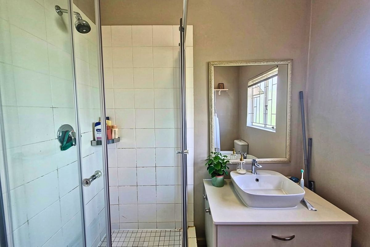 A functional bathroom featuring a glass-enclosed shower with tiled finishes and a modern vessel sink vanity unit with a wall-mounted mirror.