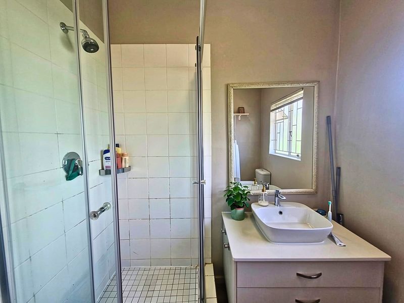 A functional bathroom featuring a glass-enclosed shower with tiled finishes and a modern vessel sink vanity unit with a wall-mounted mirror.
