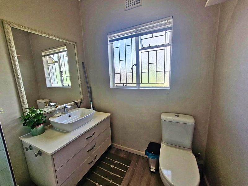 A functional bathroom featuring a modern vessel sink on a vanity cabinet, a toilet, and a window with security bars.