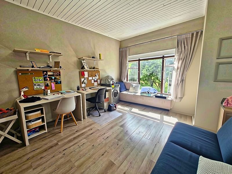 A well-lit bedroom featuring laminate flooring, a built-in window seat, and a unique tongue and groove ceiling, offering a comfortable and functional living space.